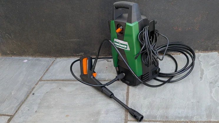 Hawksmoor High Pressure Washer 108 bar standing against a dark wall on grey paving, with its hose looped around the trigger gun and lance.