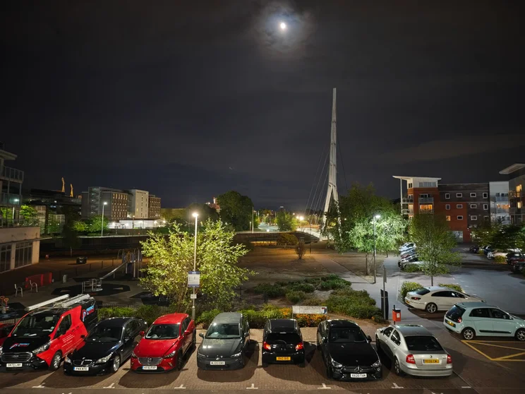 A car park at night with buildings beyond