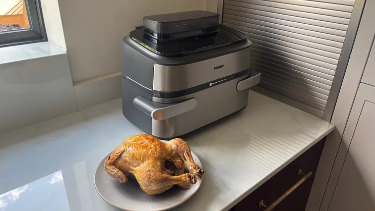 The Philips Airfryer 5000 Series Megabasket with Steam on a kitchen worktop, alongside a cooked chicken on a plate