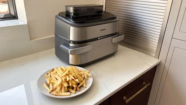 The Philips Airfryer 5000 Series Megabasket with Steam on a kitchen worktop, alongside a plate of cooked chips