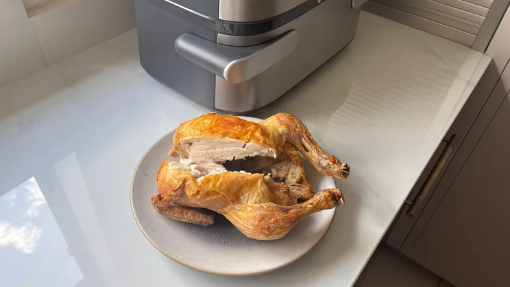 A cooked chicken on a plate, in front of the Philips Airfryer 5000 Series Megabasket with Steam, on a kitchen worktop