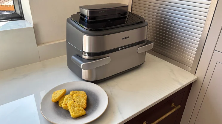 The Philips Airfryer 5000 Series Megabasket with Steam on a kitchen worktop, alongside a plate of cooked hash browns