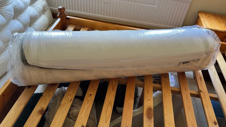 The REM-Fit Pocket 1000 Hybrid mattress, rolled up and vacuum sealed, lying across a wooden bedframe