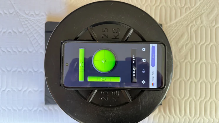 A smartphone on top of a stack of weights and a notebook, being used to test tilt at the edge of the REM-Fit Pocket 1000 Hybrid mattress