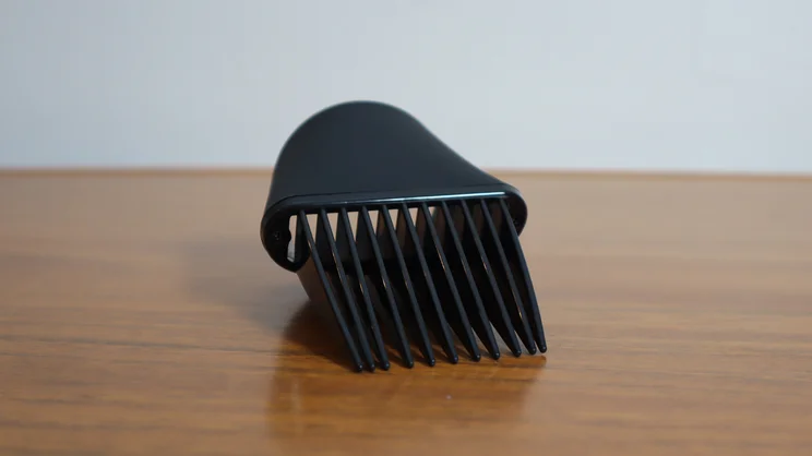 A closeup of the Revlon One Step Power Move hair dryer's root lift comb attachment, on a wooden table