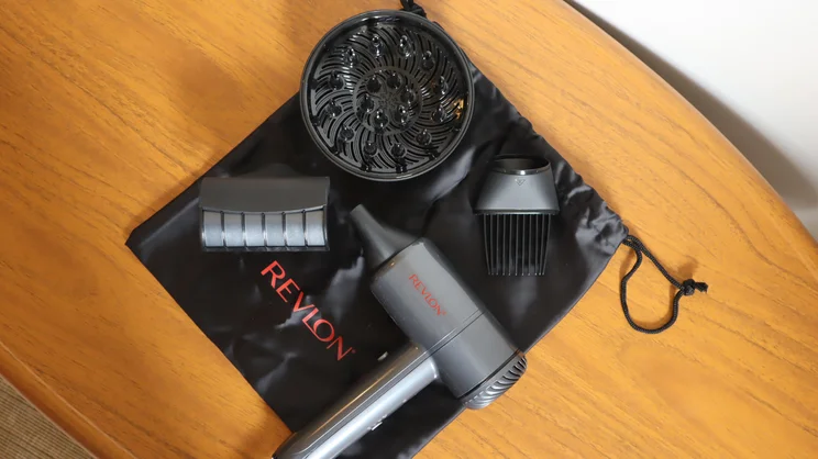 A bird's eye view of the Revlon One Step Power Move hair dryer, and its attachments, on top of its drawstring bag on a wooden table
