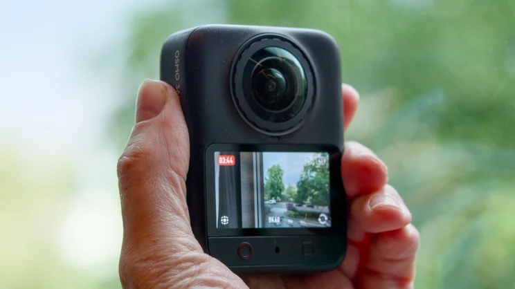 The DJI Osmo 360 II pictured being held in hand, from the rear, upright