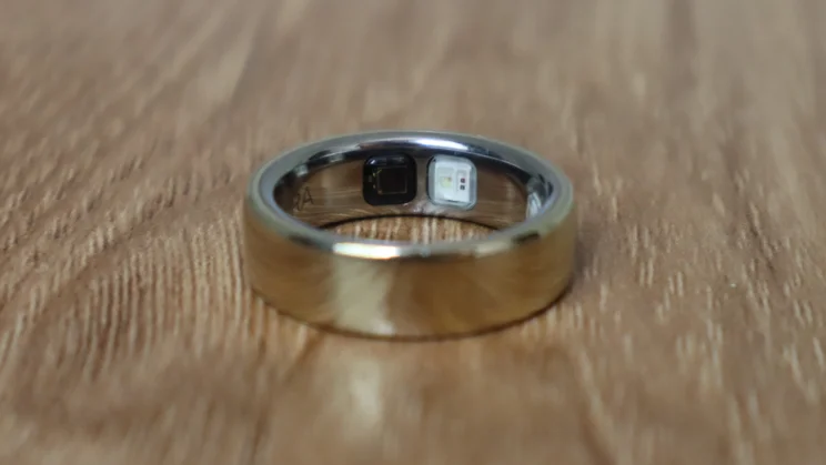 The Oura ring 5 pictured on its side on a wood table, focussing on the sensor