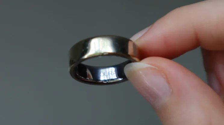 The Oura ring being held between someone's forefinger and thumb