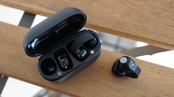 The Sennheiser Accentum Clip on a wooden chair: one earbud outside the charging case