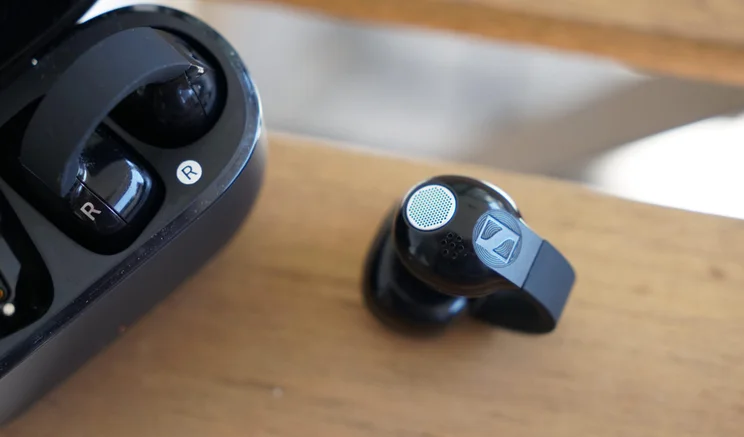 The Sennheiser Accentum Clip on a wooden slat with a close-up on a single bud outside the charging case