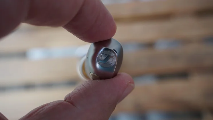 One of the Sennheiser Momentum True Wireless 5 earbuds being held to show off the Sennheiser logo