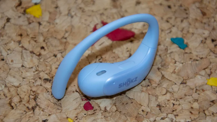 One Shokz OpenFit Air 2 earbud on a cork table with the touch-sensitive button visible