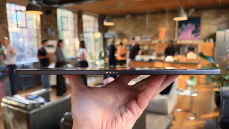 Edge-on view of the Alexa Tablet 12 Pro held flat in one hand, showing its slim profile and four keyboard connector pins.
