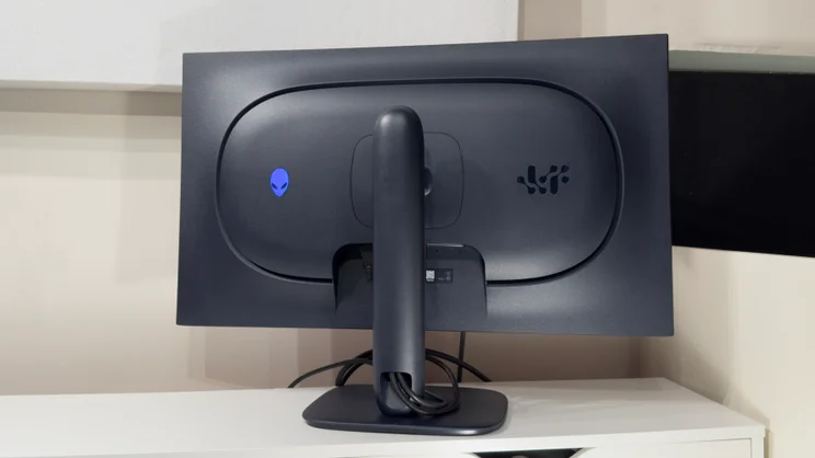 Rear view of the Alienware AW3226Q gaming monitor, showing the glowing blue alien-head logo on the back panel and cables routed through the stand's neck.