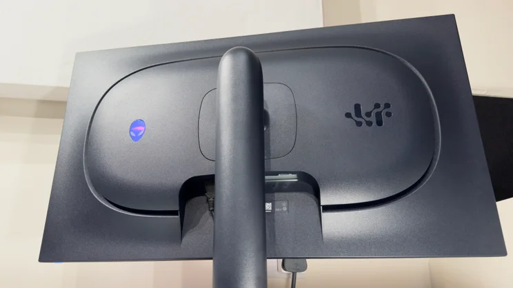 Low-angle close-up of the back of the Alienware AW3226Q gaming monitor, showing the blue alien logo, vented panel design and the power cable connection.