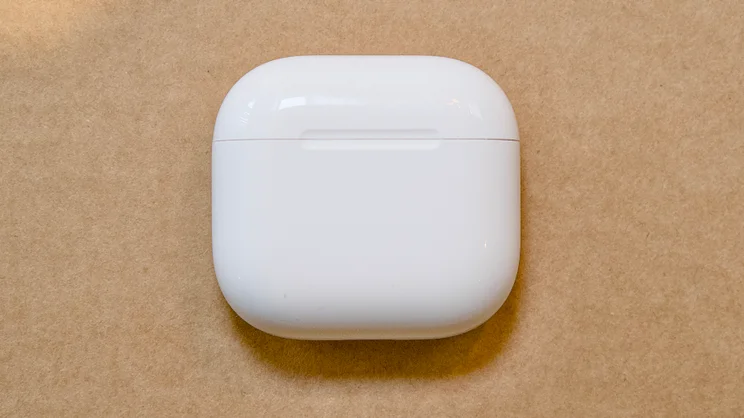 Apple AirPods 5 white charging case with the lid closed, seen from above on a brown cardboard surface