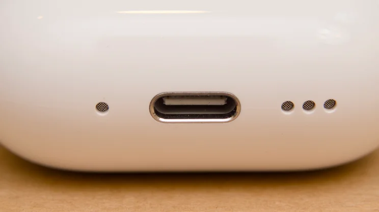 Extreme close-up of the USB-C port on the Apple AirPods 5 charging case, with a small mesh opening on the left and three on the right