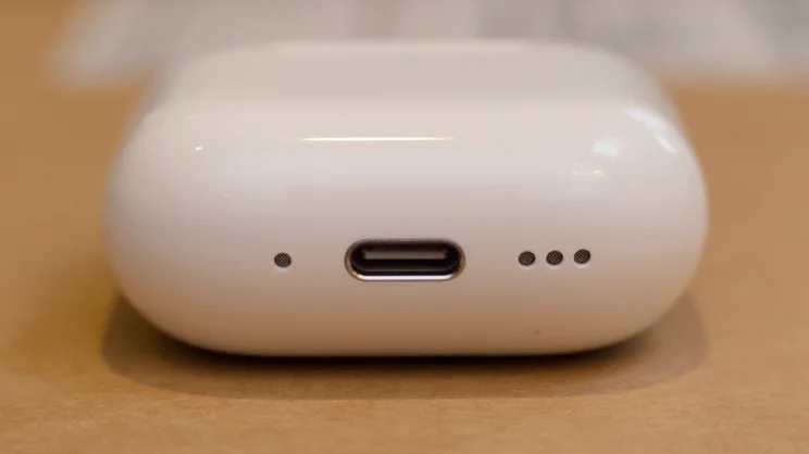 Apple AirPods 5 charging case standing on its end to show the USB-C port, with the small mesh openings on either side