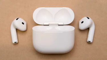 Apple AirPods 5 open charging case in the centre with the left and right earbuds lying on either side of it