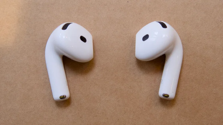 Pair of Apple AirPods 5 earbuds side by side, showing the speaker mesh, sensor openings, stems, metal contacts and faint L and R markings