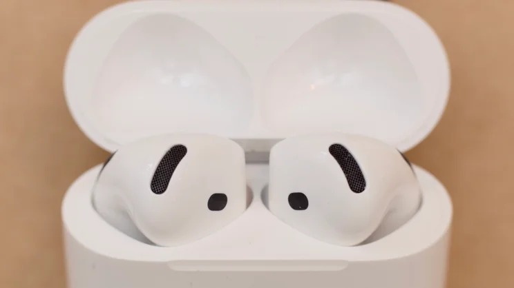 Close-up of the Apple AirPods 5 earbuds sitting in the open charging case, showing the mesh microphone vents and black sensor openings