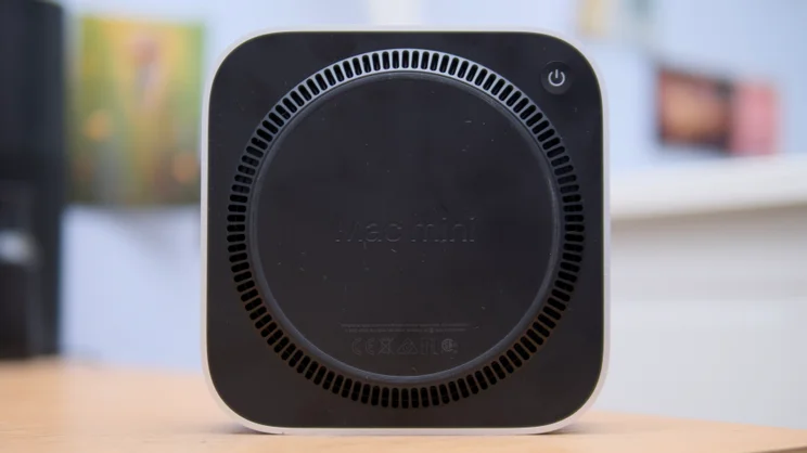 The Apple Mac mini (M5 Pro, 2026) underside, with its circular black ventilation grille and power button in close-up.