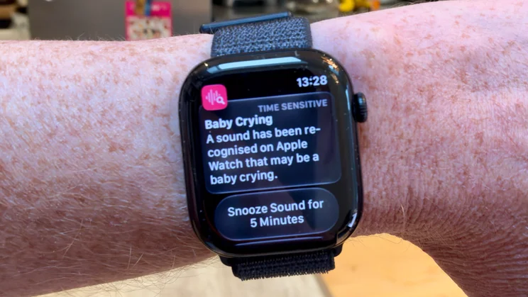 Apple Watch Series 12 on a wrist showing a time-sensitive Baby Crying sound recognition alert with a Snooze Sound for 5 Minutes button.