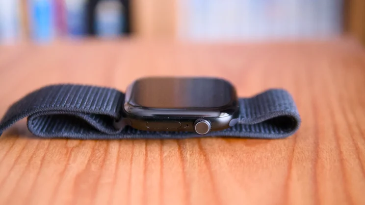 Side view of an Apple Watch Series 12 on a wooden surface, showing the Digital Crown and side button.