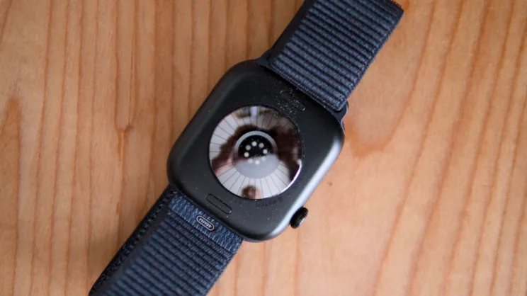 Back of an Apple Watch Series 12 on a wooden table, with a 46mm label on the Sport Loop band and sensor reflections.