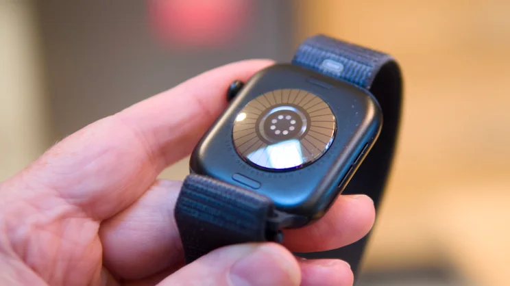Back of an Apple Watch Series 12 held between fingers, showing the ceramic and glass heart sensor array.