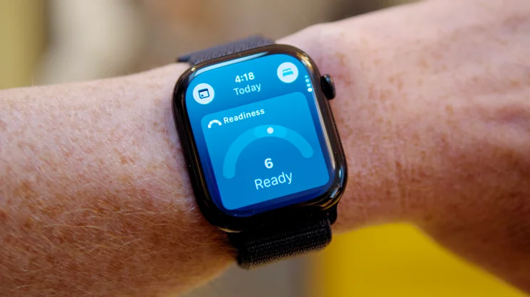 Apple Watch Series 12 on a wrist showing a Readiness score of 6, labelled Ready, on a blue screen.