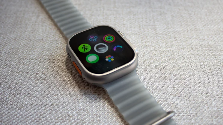 Apple Watch Ultra 4 on woven fabric showing a cluster of app icons, including Workout, Messages, Activity rings, and Readiness