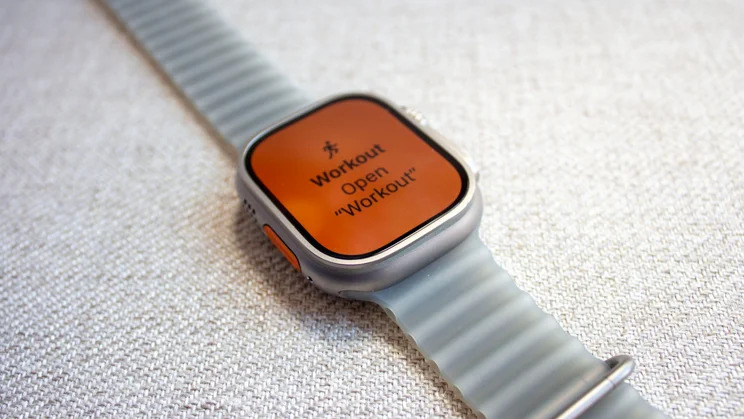 Apple Watch Ultra 4 on woven fabric with an orange screen showing a Workout prompt triggered by the Action button