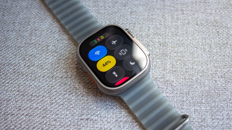 Apple Watch Ultra 4 on woven fabric showing the Control Centre, with Wi-Fi, a yellow 44% battery tile, airplane mode, flashlight and Do Not Disturb buttons