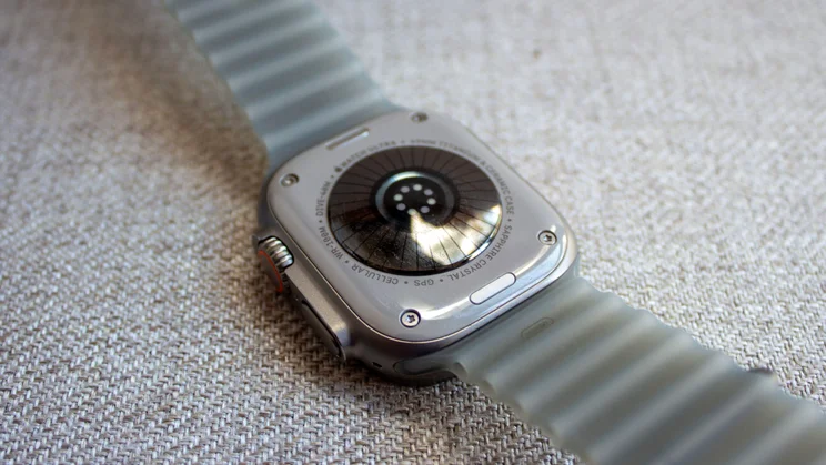 Back of the Apple Watch Ultra 4 showing the new heart rate sensor, on a woven fabric surface.