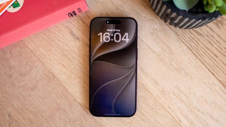 iPhone 18 Pro lying flat on a wooden table, showing its lock screen with the same swirl wallpaper and time