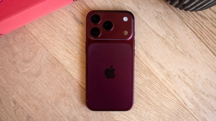 Back of a burgundy iPhone 18 Pro lying flat on a wooden table, showing the camera module and centered Apple logo