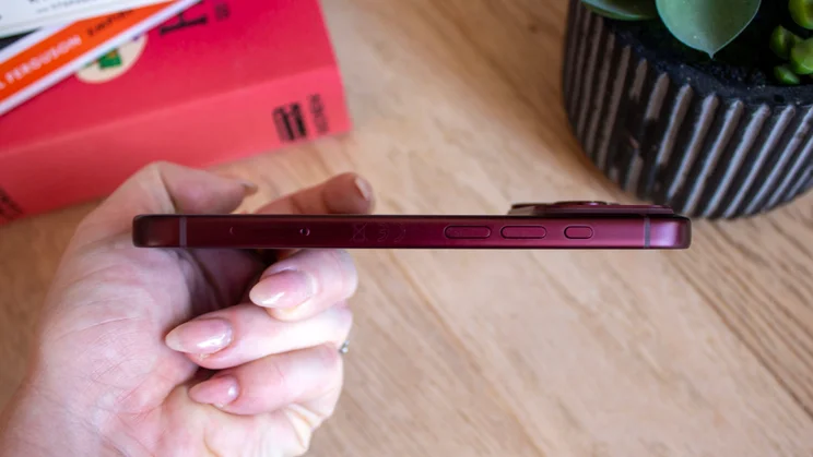 Side view of a burgundy iPhone 18 Pro held in a closed hand, showing the volume and action buttons along the edge