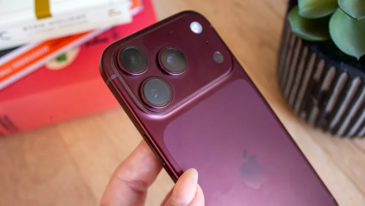 Close-up of a burgundy iPhone 18 Pro's triple-camera module and Apple logo, held near the bottom edge