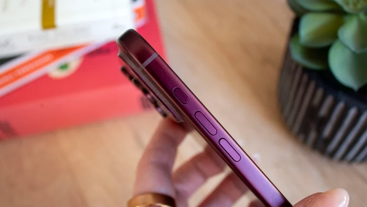 Close-up of the side edge of a burgundy iPhone 18 Pro, showing the volume buttons against a blurred plant background