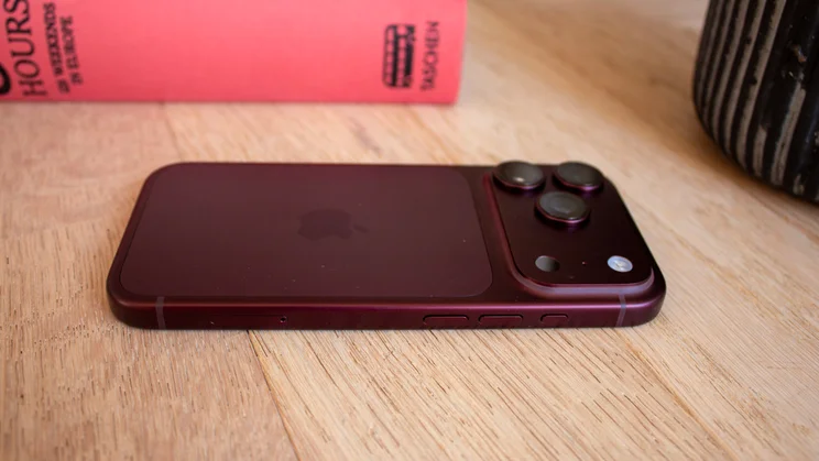 Burgundy iPhone 18 Pro lying on its side on a wooden table, showing the triple-camera module from an angle