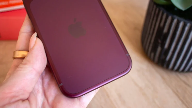 Close-up of the top corner of a burgundy iPhone 18 Pro's back panel and Apple logo, held between fingers