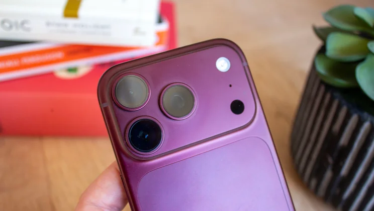 Overhead close-up of the iPhone 18 Pro's triple-camera module with flash and microphone, a potted plant blurred in the background