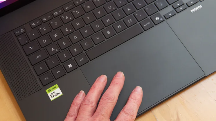 Top-down view of the Asus ProArt P16 RTX Spark laptop keyboard and wide touchpad with a hand resting on the touchpad, showing the UK key layout and the RTX Spark sticker.