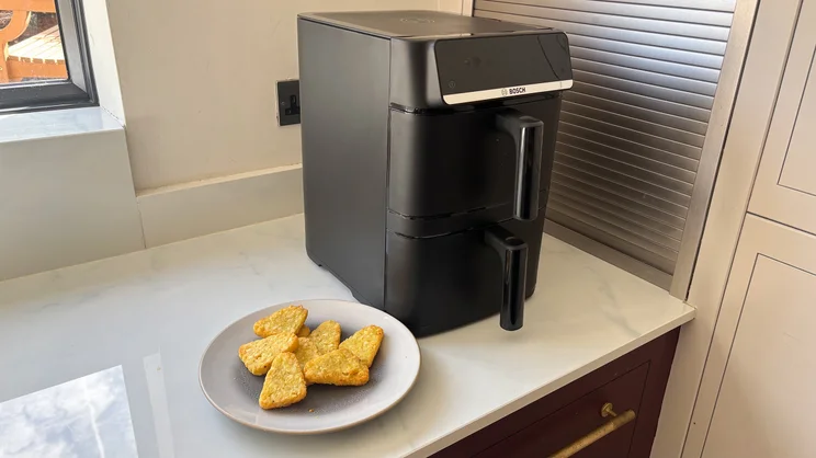 The Bosch Series 6 Double Stack Drawer Air Fryer on a kitchen worktop, next to a plate of cooked hash browns