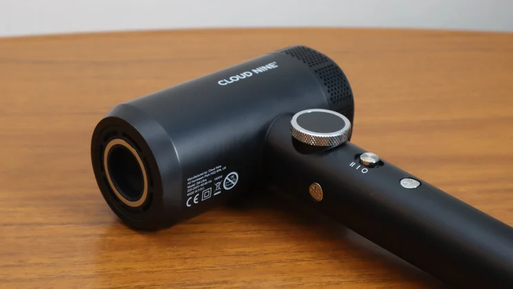 A closeup of the Cloud Nine Airshot Pro Adapt hair dryer, on its side on a wooden table