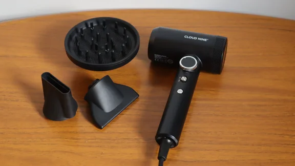 The Cloud Nine Airshot Pro Adapt hair dryer on a wooden table, alongside its attachments