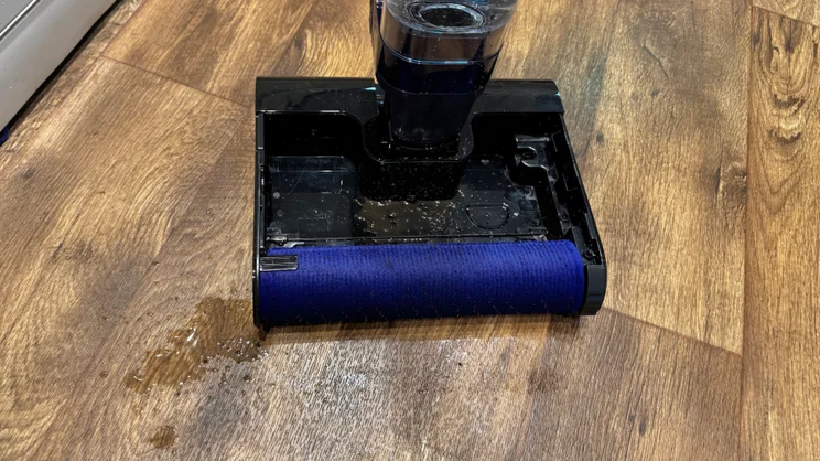 Dyson Clean and Wash Hygiene cleaner head with the blue microfibre roller exposed, and wet patches and water droplets on the floor beside it