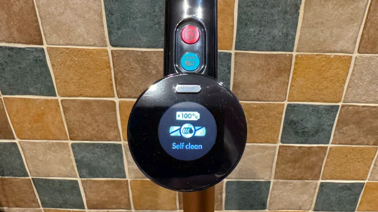 Handle display on the Dyson Clean and Wash Hygiene showing 100% battery and the self clean icon, above the red power button and blue MAX button